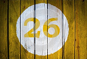 House number or calendar date in white circle on yellow toned wooden door background. Number 26 twenty six