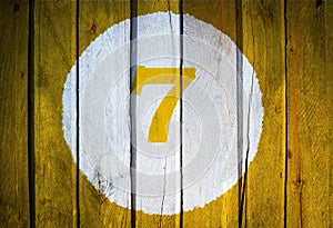 House number or calendar date in white circle on yellow toned wooden door background. Number seven 7