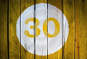 House number or calendar date in white circle on yellow toned wooden door background. Number thirty 30