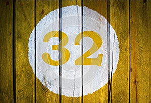 House number or calendar date in white circle on yellow toned wooden door background. Number thirty two 32
