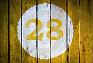 House number or calendar date in white circle on yellow toned wooden door background. Number twenty eight 28