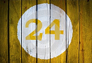 House number or calendar date in white circle on yellow toned wooden door background. Number twenty four 24