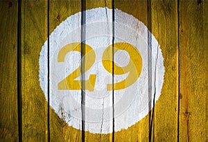 House number or calendar date in white circle on yellow toned wooden door background. Number twenty nine 29