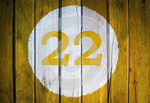House number or calendar date in white circle on yellow toned wooden door background. Number twenty two 22