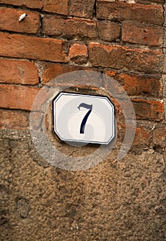 House number plaque on old brick wall. House number 7 on building. May 2013. Pisa, Italy. High quality photo