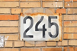 House number 245 two hundred and forty five a rusty white metal plate on an old brick wall