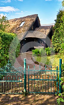 House with an old thatched roof and a wooden seating area behind the garden fence with a metal entrance gate