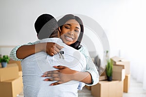 House ownership. Smiling black lady holding house key and hugging her husband, copy space