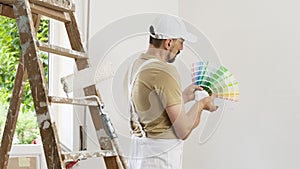 House painter man decorator choose the color using the sample swatch, work the white wall of the house to renovate, a wooden