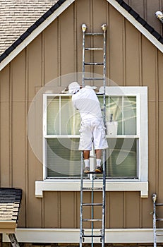 House painter paints the facade of a house standing on a ladder