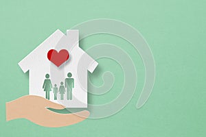 house paper cut with family icon inside and red heart over hands on grunge green background including copy space