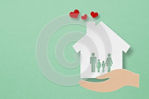 House paper cut with family icon inside and red heart over hands on grunge green background including copy space