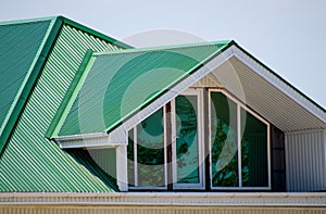 The house with plastic windows and a green roof of corrugated sheet. Green roof of corrugated metal profile and plastic windows