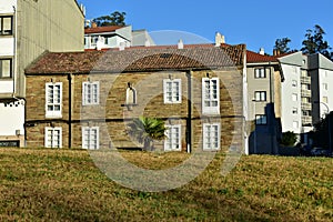 House with stone bricks, white wood windows, roof tiles and palm tree. Public park, sunny day, blue sky.