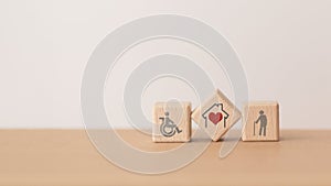 house and red heart inside wooden cube block and elderly and disability person icon, including copy space, for home or nursing