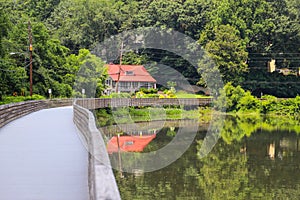 A house with a red roof along the Chattahoochee river with a long winding boardwalk with a wooden fence with lush green trees