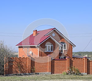 house with a red roof and red brick. Red brick fence. Roof of metal.