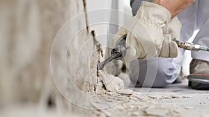 House renovation concept, construction worker breaks the old plaster of the wall with pneumatic air hammer chisel, close up with