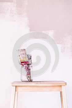 House repair, paintbrushes in glass with painted wall in the background