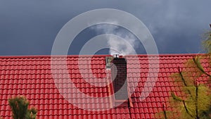 House roof with brick chimney emitting dense smoke against the sky