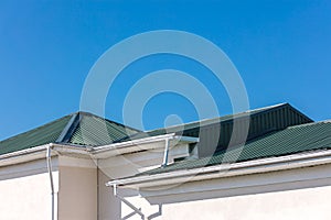 House roof with new gutter system and downspouts on blue sky background
