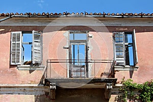 House ruins front wall with cracked destroyed facade and balcony with clear blue sky in background also seen through doors and
