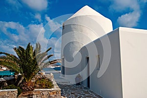 House by sea in Mykonos, Greece. Whitewashed building and palm on sunny blue sky. Typical house architecture and design
