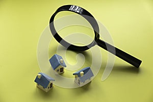 House searching concept. House inspection. Miniature house with magnifying glass over a yellow background