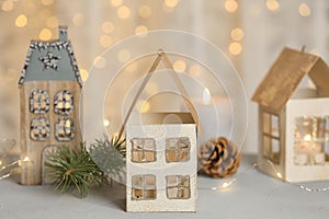 House shaped holders with burning candles on table against blurred Christmas lights