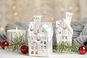 House shaped holders with burning candles on wooden table against blurred Christmas lights