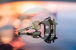 House shaped keys on reflective surface with blurred vibrant colors, symbolizing homeownership at dusk photo