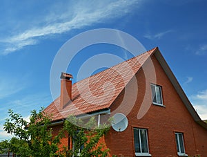 A house of simple construction built from red bricks with a metal gabled roof  a chimney  roof gutters  an attic window  and a