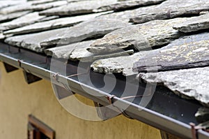 House with sloping roof, particular texture with slabs of stones and rain gutter.