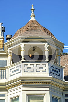 House spire or turret with metal tip and white balcony with accent paint and wooden pannels in midday sun with blue sky