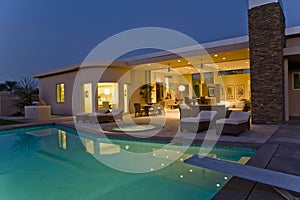 House With Sunloungers On Patio By Pool At Dusk