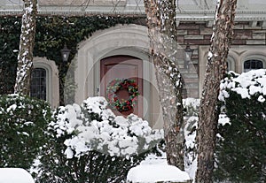 House surrounded by snow-covered evergreen bushes and with wreath on front door