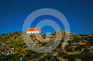 House on top of hilly landscape with bushes and rocks