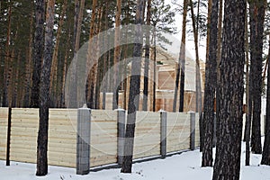 house under construction made of wooden beams in the forest fenced with a wooden fence