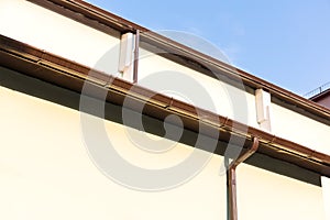 House wall with gutter and drainpipe on blue sky background