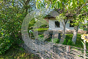 A house with white, whitewashed walls thatched roof and neat windows standing in a courtyard on a green grass fenced