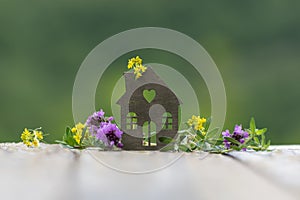 House with wild flowers on background of green nature. Eco-friendly home, gardening, real estate, ecologically pure area