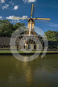 House and wooden yellow windmill next to wide tree-lined canal on the bright light of sunset at Weesp.