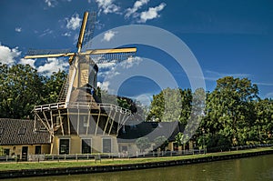 House and wooden yellow windmill next to wide tree-lined canal on the bright light of sunset at Weesp.