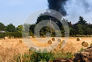Housefire in the distance after a field of rolled Hay