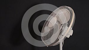 Household fan slows down and stops. Moving fan to keep cool air. Video on dark background