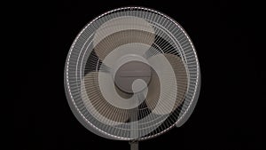 Household fan slows down and stops. Moving fan to keep cool air. Video on dark background