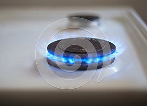 A household gas burner on a white stove burns with a blue flame. Close-up view