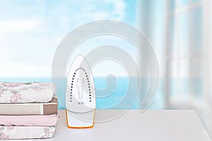 Household laundry ironing. Close-up of a yellow electrical iron and a stack of ironed clothes on an ironing board indoors over