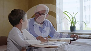 Household memories, small attractive boy with his elderly granddad have fun looking at an photo album