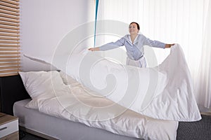 Housekeeper Arranging Bedsheet On Bed